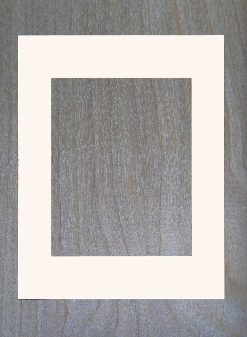 May include: A white picture frame with a thick white mat. The frame is on a wood background.
