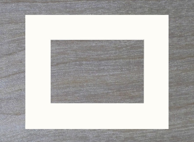 May include: A white picture frame with a white mat, creating a double border around the opening. The frame is on a woodgrain background.