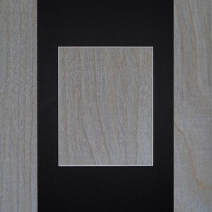 May include: A black picture frame with a white mat, creating a double border around a blank space in the center. The frame is on a light wood background.