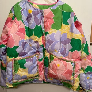 May include: A green, pink, and purple floral print quilted jacket with two patch pockets. The jacket has a button closure and a pink lining.