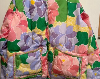 May include: A green, pink, and purple floral print quilted jacket with two patch pockets. The jacket has a button closure and a pink lining.
