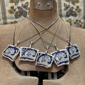 May include: Five blue and white ceramic pendants with silver chains hanging from a mannequin's neck. Each pendant features a unique design with a blue and white pattern.