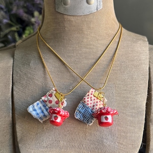 May include: Two gold chain necklaces with red and blue patchwork fabric mushroom charms. The charms have a white and red strawberry design.