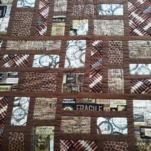 May include: A brown and tan quilt with a patchwork design. The quilt features various images, including coffee beans, clocks, and cigars. The quilt is made of different fabrics and textures.
