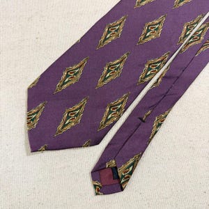 May include: A purple necktie with a repeating diamond pattern. Each diamond features a gold border with green and red accents. The tie is made of a smooth fabric and is suitable for formal or business attire.