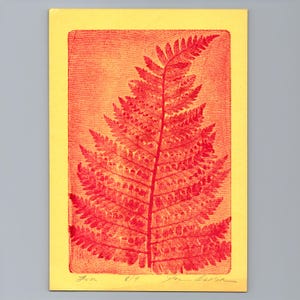 May include: A rectangular print on yellow paper featuring a detailed red fern leaf illustration. The artwork displays a textured background with fine horizontal lines and handwritten pencil markings at the bottom edge, including the title and signature.