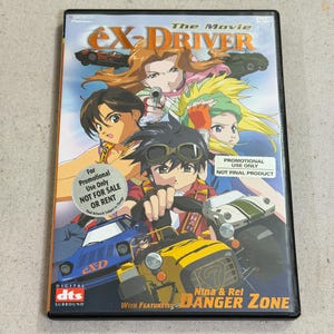 May include: A DVD case for the anime movie eX-Driver: Nina & Rei Danger Zone. The cover features three characters, a yellow race car, a blue car, and a white car. Text includes "The Movie", "eX-Driver", "For Promotional Use Only", and "DTS".