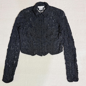 May include: Black, cropped jacket with intricate floral embroidery and small bead accents. The jacket features long sleeves, a collared neckline, and a button-up front. The label "bebe" is visible on the collar.