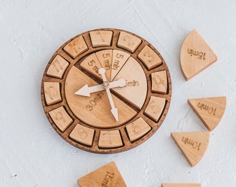 May include: A circular wooden clock learning tool with engraved numbers 1 through 12 around the perimeter. The center features movable clock hands and removable wedge-shaped wooden pieces labeled with time increments like 5min, 10min, 15min, and 30min.