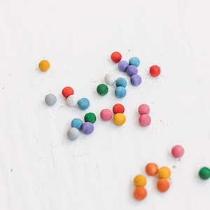 May include: A collection of colorful wooden balls in various shades of blue, green, red, orange, yellow, and purple scattered on a white surface.