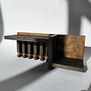 May include: A wall-mounted wooden shelf unit featuring a combination of dark black and natural brown wood finishes. The structure includes a long horizontal shelf supported by vertical slats and a separate, lower flat surface section.