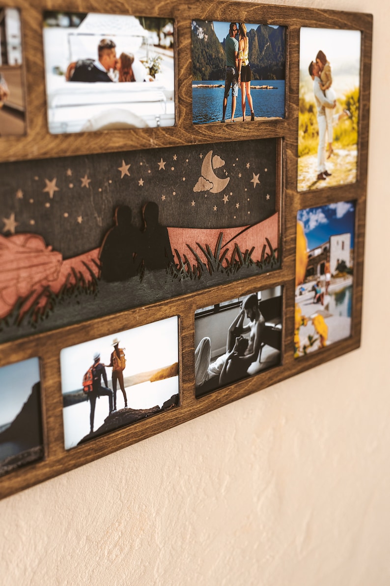 May include: A dark brown wooden multi-photo frame featuring a central decorative panel with a laser-cut night sky scene, including a crescent moon, stars, and two silhouettes sitting in grass, surrounded by seven rectangular photo display slots.