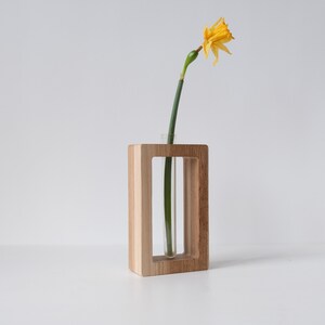 May include: A wooden vase with a clear glass tube for holding a single flower. A yellow daffodil is in the vase.
