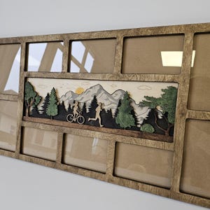 Könnte beinhalten: Ein Bilderrahmen aus Holz mit 10 Öffnungen für Fotos. Der Rahmen hat ein geschnitztes Design einer Bergszene mit Bäumen, einem Paar auf einem Fahrrad und einer laufenden Person. Der Rahmen ist braun mit einer natürlichen Holzoptik.