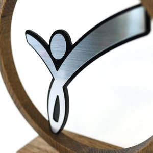 May include: A silver and black stylised figure of a person with outstretched arms, mounted on a wooden base.