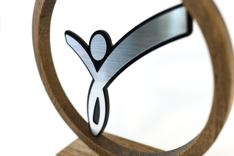 May include: A silver and black stylised figure of a person with outstretched arms, mounted on a wooden base.