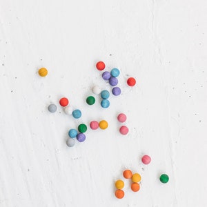 May include: A collection of colorful wooden balls scattered on a white surface. The balls are in various shades of blue, green, red, orange, and yellow.