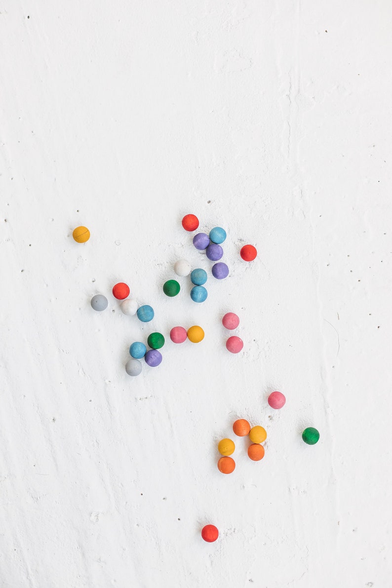 May include: A collection of colorful wooden balls scattered on a white surface. The balls are in various shades of blue, green, red, orange, and yellow.
