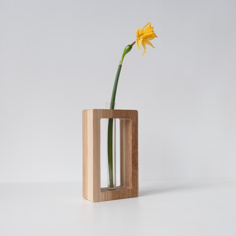 May include: A wooden vase with a clear glass tube insert, holding a single yellow daffodil.