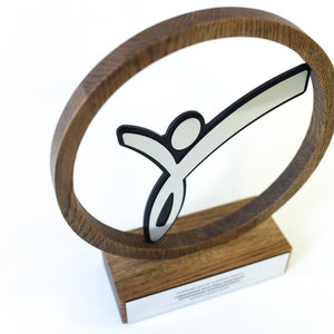 May include: A wooden award featuring a silver stylised figure of a person within a circular frame. The award has a wooden base with a silver plaque.