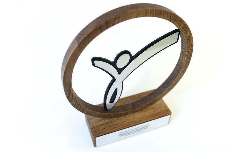 May include: A wooden award featuring a silver stylised figure of a person within a circular frame. The award has a wooden base with a silver plaque.