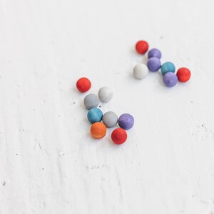 May include: A group of colorful wooden balls in shades of red, orange, blue, gray, and purple. The balls are scattered on a white surface.
