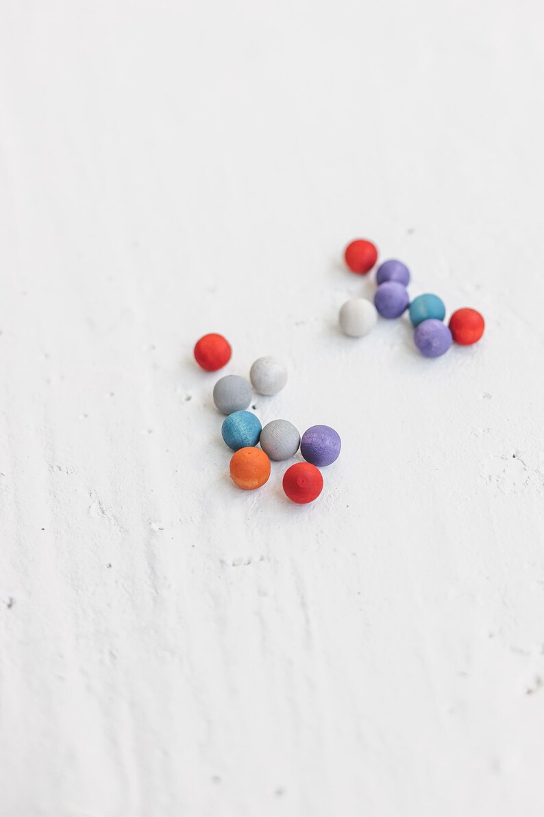 May include: A group of colorful wooden balls in shades of red, orange, blue, gray, and purple. The balls are scattered on a white surface.