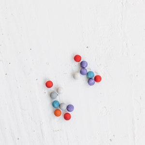 May include: A group of colorful wooden balls arranged in a pattern on a white surface. The balls are red, orange, blue, gray, and purple.
