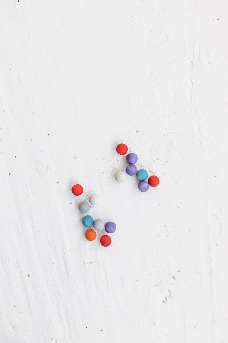 May include: A group of colorful wooden balls arranged in a pattern on a white surface. The balls are red, orange, blue, gray, and purple.