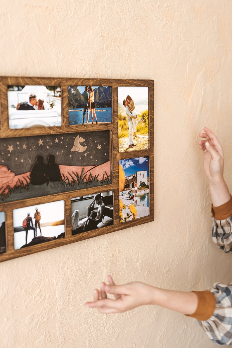 May include: A rectangular wooden multi-photo frame with a dark brown finish. The frame features six rectangular openings for photographs and a central decorative panel depicting a laser-cut silhouette of two people sitting under a moon and stars.