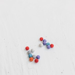 May include: A group of colorful round beads in shades of red, blue, gray, and purple are scattered on a white surface.