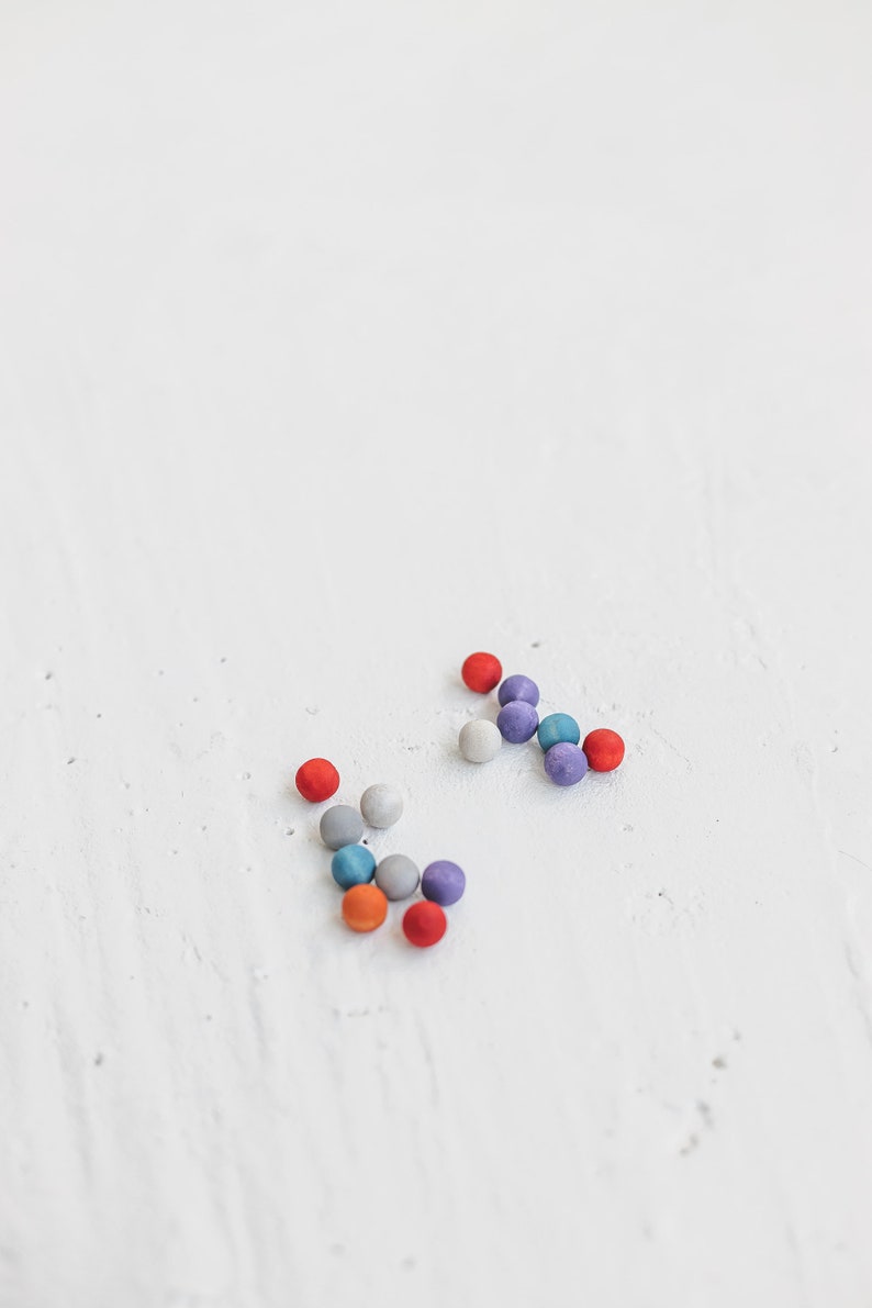 May include: A group of colorful round beads in shades of red, blue, gray, and purple are scattered on a white surface.