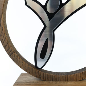 May include: A silver-coloured stylised figure of a person with black outlines, mounted on a wooden circular base. The figure is raised above the base and appears to be jumping or reaching upwards.