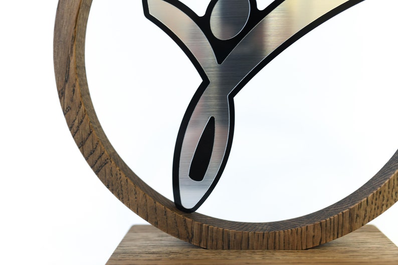 May include: A silver-coloured stylised figure of a person with black outlines, mounted on a wooden circular base. The figure is raised above the base and appears to be jumping or reaching upwards.