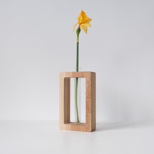 May include: A wooden vase with a clear glass tube insert, holding a single yellow daffodil flower.