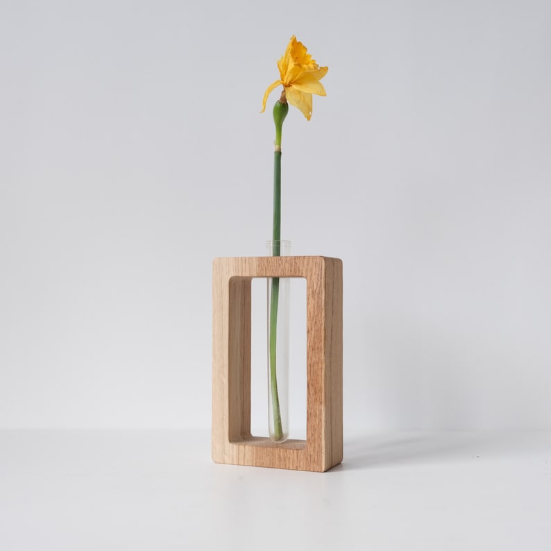 May include: A wooden vase with a clear glass tube insert, holding a single yellow daffodil flower.