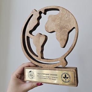 May include: A wooden globe award with a gold plaque that reads "TSGT STEPHANIE SHISHIDO 2022 Air Force Surgeon General's Commitment to DEI Award".