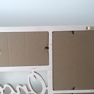 Pode incluir: Uma moldura de madeira clara para v&aacute;rias fotos com tr&ecirc;s aberturas retangulares e fundos de papel&atilde;o castanho fixados por clipes de metal preto. Um gancho de metal dourado em forma de serra est&aacute; fixado no canto superior direito.