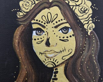 May include: Square painting of a woman with a sugar skull design. The woman has brown hair and a gold floral crown. Her face is painted with gold and black details. The background is black.