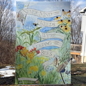 May include: A rectangular sign with the text "Never Mind the Weeds, We're Feeding the Bees" on a blue ribbon. The sign features a watercolor illustration of wildflowers, bees, and butterflies. The words "Celebrate Biodiversity" are at the bottom.