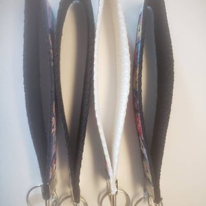 May include: Four wrist keychains with black, white, and patterned fabric straps. Each keychain has a silver-colored metal ring for attaching keys. The keychains are designed to be worn around the wrist.