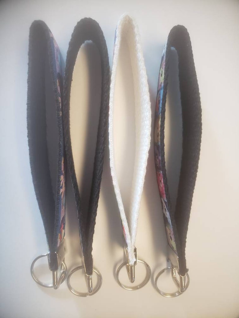 May include: Four wrist keychains with black, white, and patterned fabric straps. Each keychain has a silver-colored metal ring for attaching keys. The keychains are designed to be worn around the wrist.