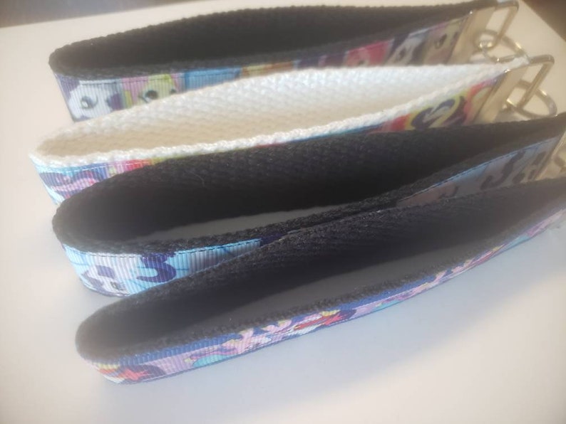May include: Three keychains with wrist straps. The straps are made of patterned ribbon with a black interior and a metal key ring. The patterns include a variety of colors, including blue, pink, and white.
