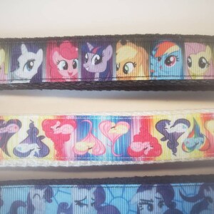 May include: Three colorful keychains featuring cartoon pony characters. The top keychain has a black border and a series of pony faces. The middle keychain has a white border with heart and pony designs. The bottom keychain has a blue border with pony faces.