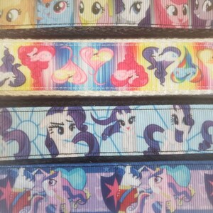 May include: Close-up of several ribbons featuring colorful cartoon pony characters. The ribbons display various designs, including pony faces, hearts, and other graphics. The ribbons are bordered with black lace.