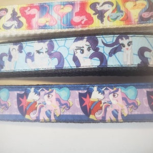May include: Three keychains with colorful cartoon pony designs. The top keychain features a rainbow pattern, the middle one has a light blue background, and the bottom one has a blue background. Each keychain has a metal clasp.