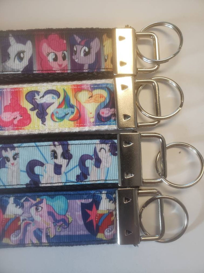 May include: Four keychains with colorful cartoon pony designs. Each keychain features a different pattern with images of the ponies. The keychains have a silver metal clasp and a key ring.