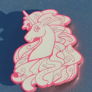 Puede incluir: Un unicornio blanco con un contorno rosa y una melena fluida. El unicornio est&aacute; representado en un estilo caprichoso con patrones en espiral en su melena.