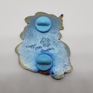 Puede incluir: Un pin de esmalte azul e iridiscente con un drag&oacute;n con una corona y el texto "Dragon Child Graphics" en la parte posterior.