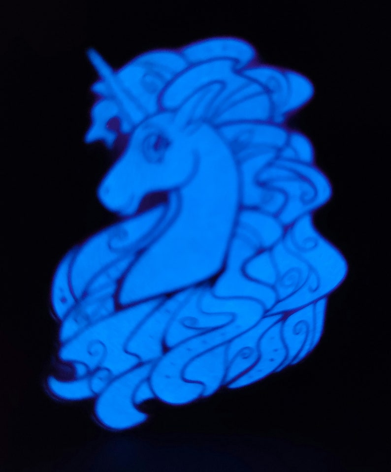 Puede incluir: Un pin de unicornio azul que brilla en la oscuridad con un dise&ntilde;o detallado. El unicornio tiene una melena y una cola fluidas, y un cuerno.